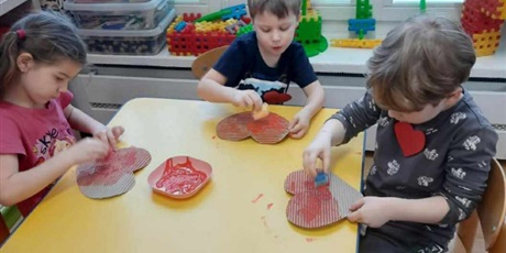 Powiększ grafikę: Dzieci siedzą przy stoliku i malują farbami czerwone serca
